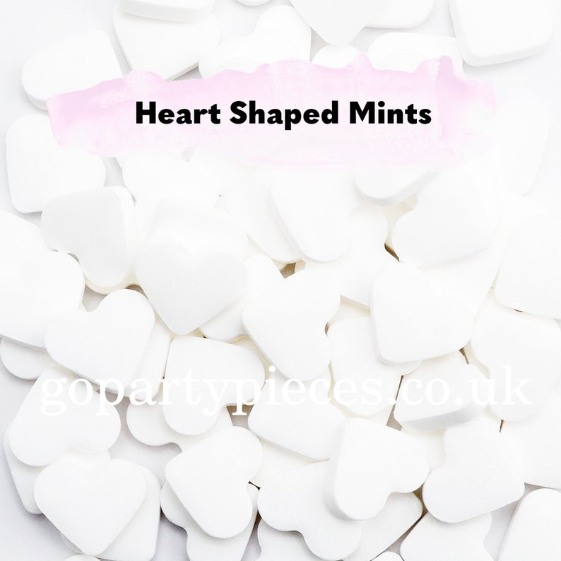Op de afbeelding: Een close-up van witte hartvormige pepermuntjes verspreid over een witte ondergrond. De afbeelding bevat de tekst "Heart Shaped Mints". Perfect voor feesten en evenementen.