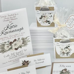 Peut inclure: Un ensemble pour une fête prénuptiale avec une invitation florale, un menu, des marque-places et des cadeaux de thé. L'invitation indique "Vous êtes invité(e) à une belle fête prénuptiale pour Katie Kavanaugh." Les cadeaux sont dans des boîtes en forme de tasse à thé.