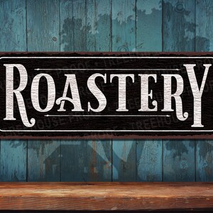 May include: Black and white sign with the word "ROASTERY" in white lettering on a black background. The sign has a rustic, distressed look.