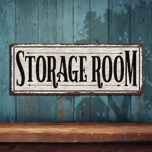 May include: A white metal sign with black lettering that reads "STORAGE ROOM" against a blue wood background.