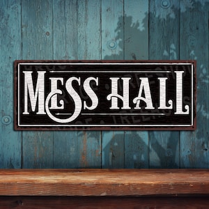 May include: Black and white metal sign with the text "MESS HALL" in a vintage style font. The sign has a distressed look and is mounted on a wooden wall.