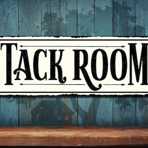 May include: A white metal sign with black lettering that reads "Tack Room". The sign has a distressed look and is hanging on a blue wooden wall.