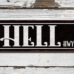 May include: A black and white metal sign with the word "HELL" in large white letters and "HWY" in smaller white letters. The sign has a rustic brown border.