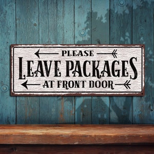 May include: White metal sign with black text and arrows that reads "Please Leave Packages At Front Door". The sign has a distressed, vintage look.
