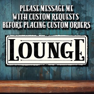 May include: A white sign with black lettering that reads "LOUNGE" on a blue wooden background. The sign has a distressed look and is framed with a black border. The text "PLEASE MESSAGE ME WITH CUSTOM REQUESTS BEFORE PLACING CUSTOM ORDERS" is written above the sign.