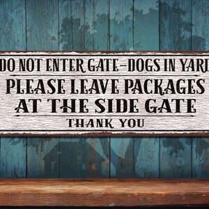 May include: A rectangular metal sign with the text "DO NOT ENTER GATE-DOGS IN YARD PLEASE LEAVE PACKAGES AT THE SIDE GATE THANK YOU". The sign has a white background with black text and a brown border.