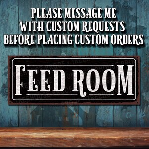 May include: A rustic brown metal sign with white text that reads "FEED ROOM". The sign is hanging on a blue wooden wall.