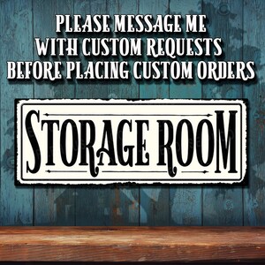 May include: A white sign with black lettering that reads "Storage Room". The sign is hanging on a blue wooden wall. The text "Please message me with custom requests before placing custom orders" is written in black on a white background above the sign.