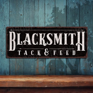 May include: Black metal sign with white text that reads "Blacksmith Tack & Feed". The sign has a rustic, weathered look.
