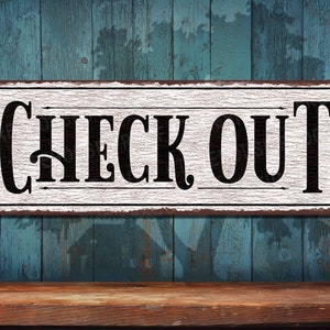 May include: A white sign with black lettering that reads "CHECK OUT" on a rustic blue wooden background.