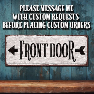 May include: A white sign with black text and arrows pointing left and right. The sign reads "Front Door". The sign is on a blue wooden background.