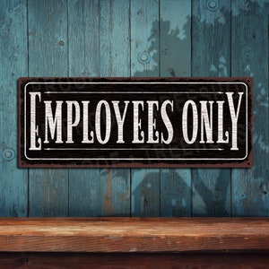 May include: A black metal sign with white text that reads "EMPLOYEES ONLY". The sign is hanging on a blue wooden wall.