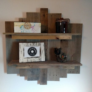 May include: A rustic wooden shelf unit with two shelves. The shelves are made of reclaimed wood and have a natural, weathered finish. The shelf unit is mounted on a white wall and has a decorative design. There are various items on the shelves, including a small box, a jar, a picture frame, and a snow globe.