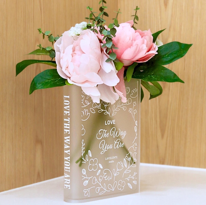 Glass flower vase in the sape of a book with pink peonies.