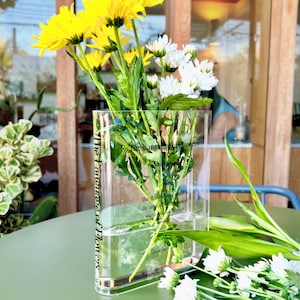 Acrylic book-shaped vase filled with vibrant flowers, placed on a modern bookshelf, perfect for home decor and gifting for events, birthdays, and housewarmings.