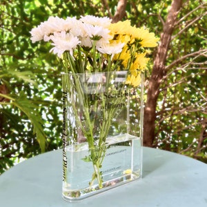 Acrylic book-shaped vase filled with vibrant flowers, placed on a modern bookshelf, perfect for home decor and gifting for events, birthdays, and housewarmings.