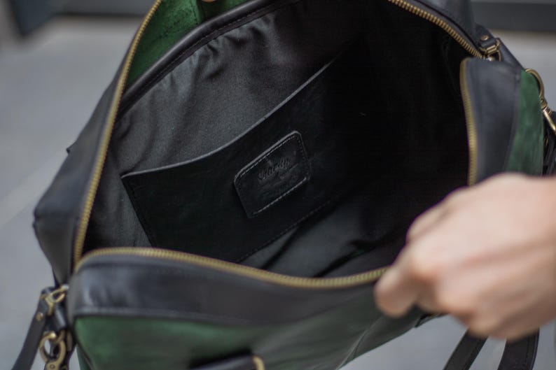 May include: Open view of a black leather bag with a green suede accent. The bag has a gold zipper and a black interior with a pocket. A small black leather tag with the word "Vintage" is visible inside the bag.