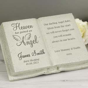 Op de afbeelding: Een wit, boekvormig gedenkteken met de tekst "Heaven has gained an Angel" en "James Smith" gegraveerd op de voorkant. De tekst "Born Sleeping 01.08.2023" is ook gegraveerd op de voorkant. De achterkant van het boek heeft de tekst "Our darling Angel Baby. Silent from the start we will never forget you you will remain always in our hearts. Love Mummy & Daddy XXXX".
