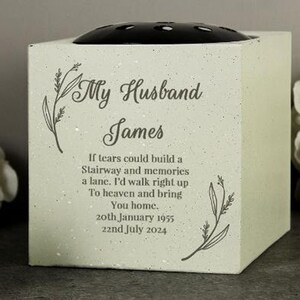 Pode incluir: Um vaso de flores memorial quadrado verde claro com um sapo floral preto. A frente do vaso tem o texto "My Husband James" e um poema com datas. Há raminhos decorativos à esquerda e à direita.