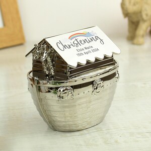 May include: Silver-plated Noah's Ark money box with a removable roof. The roof has a rainbow and clouds design and the text "Christening Elsie Marie 15th April 2024".
