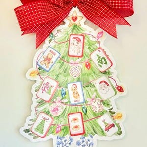 May include: A Christmas tree-shaped wall hanging featuring a watercolor illustration of a green tree in a blue and white floral vase. The tree is decorated with mahjong tiles, string lights, and a red and white checkered fabric bow at the top.