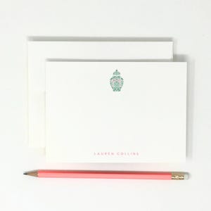 May include: White stationery set with a decorative green and pink design and the name "LAUREN COLLINS" printed in pink. A pink pencil with a gold ferrule rests below the stationery.