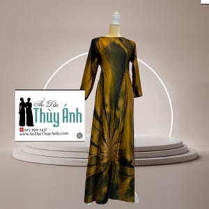 Op de afbeelding: Een lange jurk met lange mouwen, in goud en zwart, gepresenteerd op een mannequin. De jurk heeft een uniek, abstract bloemenpatroon. De afbeelding bevat een logo met tekst en silhouetten.