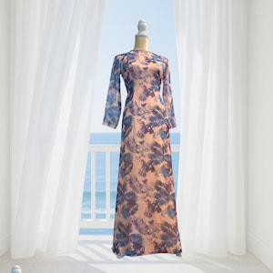 May include: A long, flowing dress with a floral pattern in shades of peach, blue, and purple. The dress has long sleeves and a round neckline. The fabric appears to be lightweight and sheer. The dress is displayed on a mannequin.