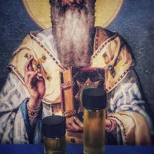 May include: Two small glass bottles with black lids, filled with a golden liquid, are displayed on a blue surface with a Masonic symbol. The background features a religious painting of a bearded man.