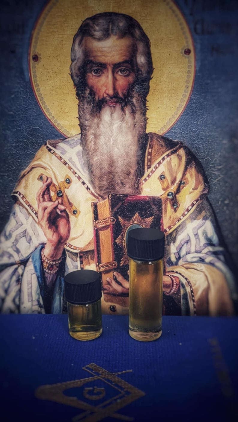May include: Two small glass bottles with black lids, filled with a golden liquid, are displayed on a blue surface with a Masonic symbol. The background features a religious painting of a bearded man.