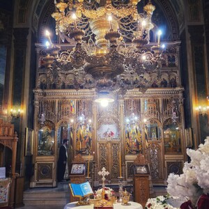 May include: Interior of a church with a large, gold chandelier and detailed wooden carvings. A table with a white lace cloth displays religious items. The walls are decorated with paintings, creating a rich, historical atmosphere.