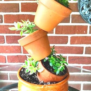 May include: A stacked arrangement of terracotta pots with green succulents. The pots are stacked in a staggered pattern, with the largest pot at the bottom and the smallest pot at the top. The pots are all brown and have a rough texture. The succulents are green and have a variety of shapes and sizes.