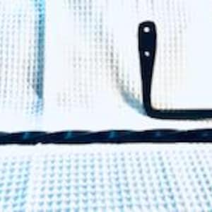 May include: Black metal towel rack with a twisted design. The rack is mounted to a wall and has a curved arm for hanging towels.