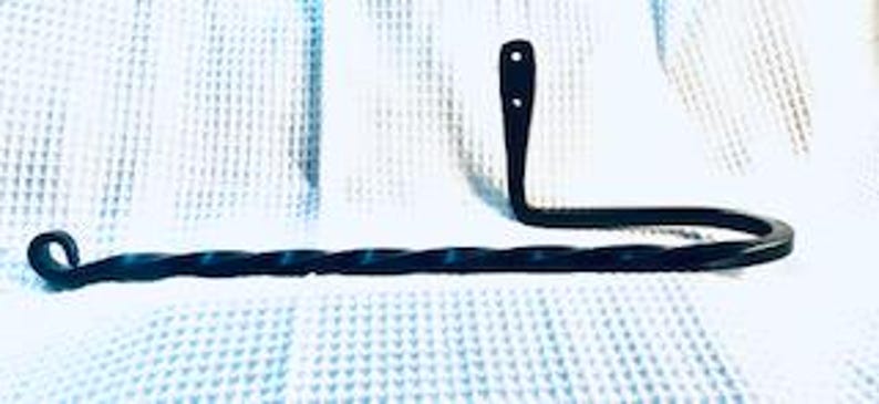 May include: Black metal towel rack with a twisted design. The rack is mounted to a wall and has a curved arm for hanging towels.