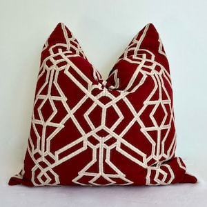 May include: A burgundy pillow with a geometric pattern embroidered in cream. The pattern is a series of interlocking squares and diamonds.