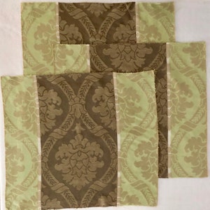 May include: Three brown and green fabric placemats with a damask pattern. The placemats have a light green border and a brown center with a repeating pattern.