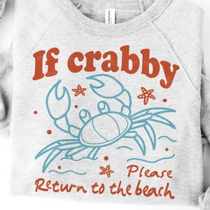 May include: A light gray sweatshirt with the text "If crabby Please Return to the beach". The design features a blue crab illustration with red text and accents. The sweatshirt is folded.