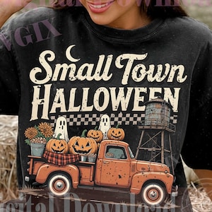 May include: A black t-shirt featuring a graphic of an orange vintage pickup truck carrying pumpkins and two ghosts. The text reads Small Town HALLOWEEN. The design includes a water tower, a checkered pattern, and a crescent moon in a retro style.