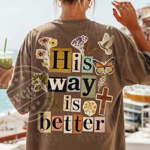 Könnte beinhalten: Braunes T-Shirt mit dem Text "His way is better" im Collage-Stil, verziert mit Blumen- und Schmetterlingsmotiven. Das Shirt hat eine lockere Passform und kurze Ärmel.