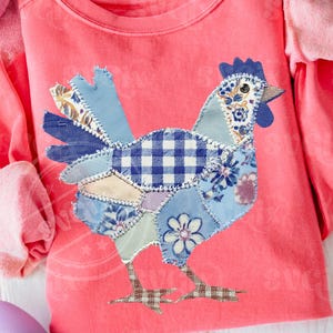 May include: A coral-colored long-sleeved shirt featuring a patchwork chicken design. The chicken is composed of various blue patterned fabrics, including floral and gingham patterns. The shirt has a crew neck and long sleeves, perfect for casual wear.