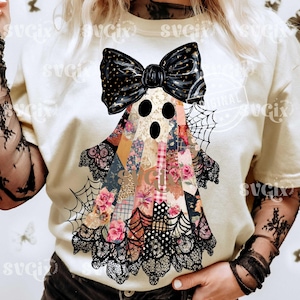 以下が含まれることがあります： クリーム色のTシャツ。大きな黒いリボンとパッチワークのボディが特徴のゴーストデザイン。ゴーストの体は花柄や模様の生地で飾られ、黒いレースとクモの巣が特徴です。ハロウィーンに最適です。