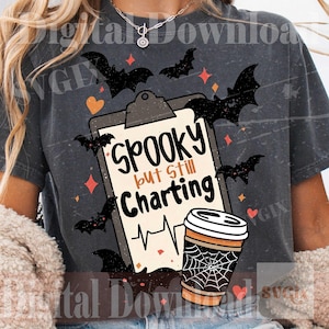 May include: A charcoal gray t-shirt featuring a graphic of a clipboard with the text Spooky but Still Charting, a heart rhythm line, a coffee cup with a spiderweb design, and black bats, orange hearts, and small diamond shapes.