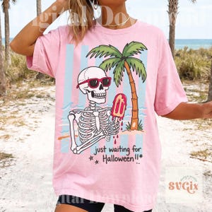 May include: Pink t-shirt featuring a skeleton wearing sunglasses and holding a melting popsicle in front of a palm tree and beach scene. The text "just waiting for Halloween!!" is below the graphic.