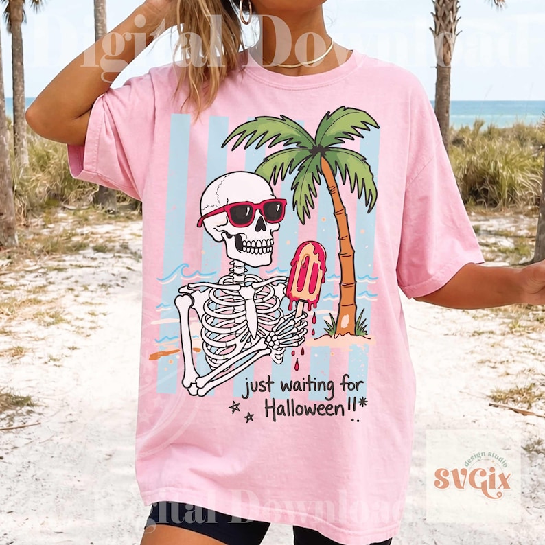 May include: Pink t-shirt featuring a skeleton wearing sunglasses and holding a melting popsicle in front of a palm tree and beach scene. The text "just waiting for Halloween!!" is below the graphic.