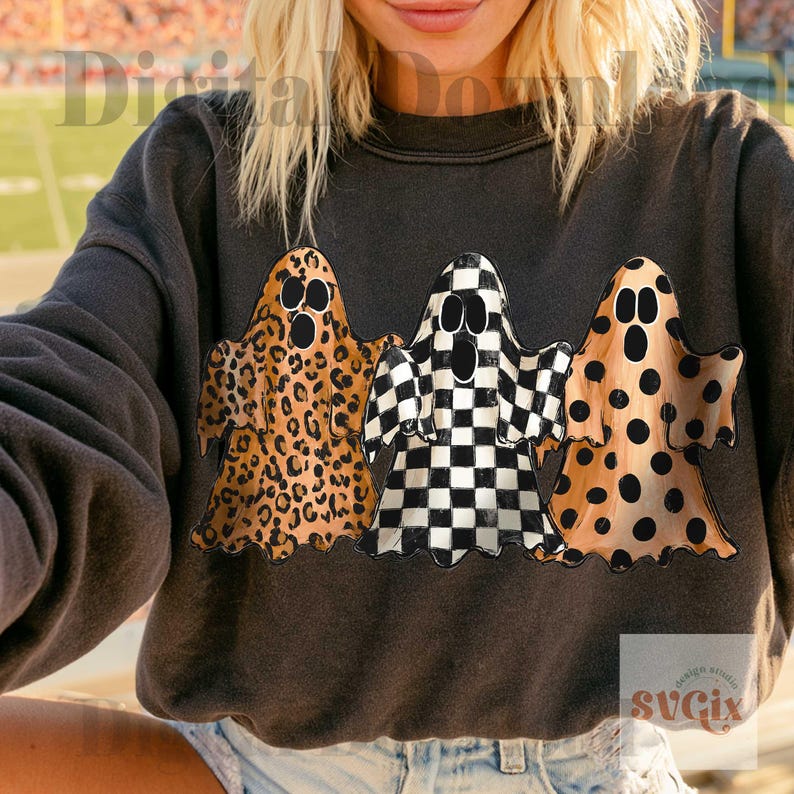 May include: A dark charcoal gray crewneck sweatshirt featuring a graphic of three ghosts. The left ghost has a brown leopard print, the center ghost has a black and white checkerboard pattern, and the right ghost has a tan base with black polka dots.