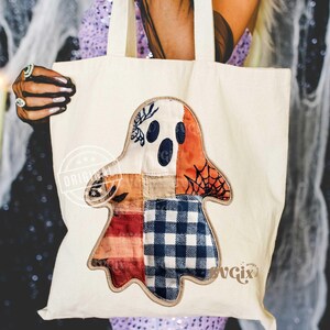 May include: Cream-colored tote bag featuring a patchwork ghost design. The ghost has a white face with blue eyes, an orange head, and a body made of plaid and patterned fabrics. The bag has sturdy handles and is perfect for carrying groceries or books.