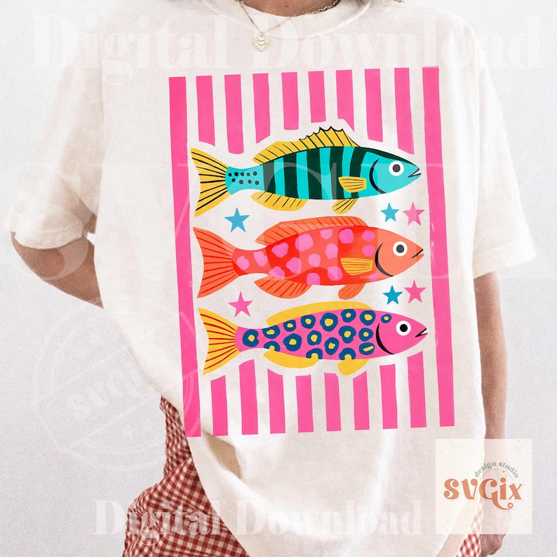 May include: White t-shirt featuring a colorful graphic of three stylized fish. The fish are in shades of blue, orange, and pink, with yellow fins and patterned details. The design includes pink vertical stripes and stars.