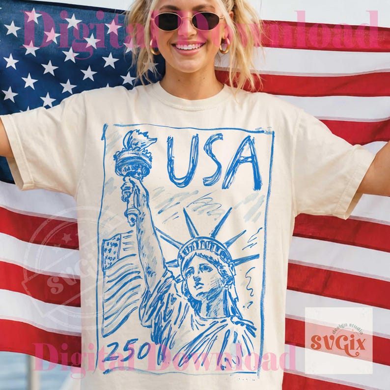 K&ouml;nnte beinhalten: Cremefarbenes T-Shirt mit einer blauen Skizze der Freiheitsstatue und dem Wort "USA". Die amerikanische Flagge ist im Hintergrund. Das T-Shirt-Design enth&auml;lt die Zahl "250".