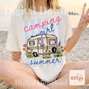 May include: Cream t-shirt featuring a campervan graphic with the words "camping girl summer." The design includes a pink bow, blue stripes, and flowers. The overall style is retro and summery.