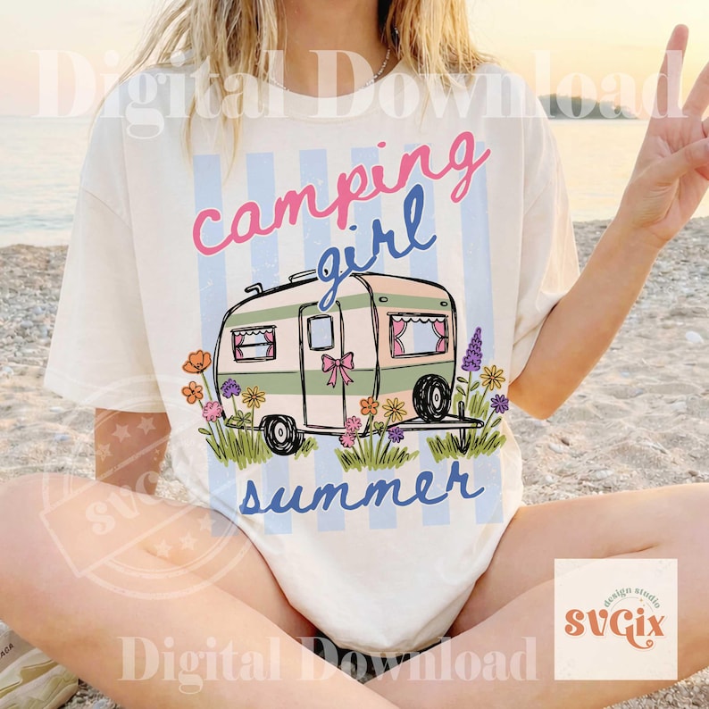 May include: Cream t-shirt featuring a campervan graphic with the words "camping girl summer." The design includes a pink bow, blue stripes, and flowers. The overall style is retro and summery.